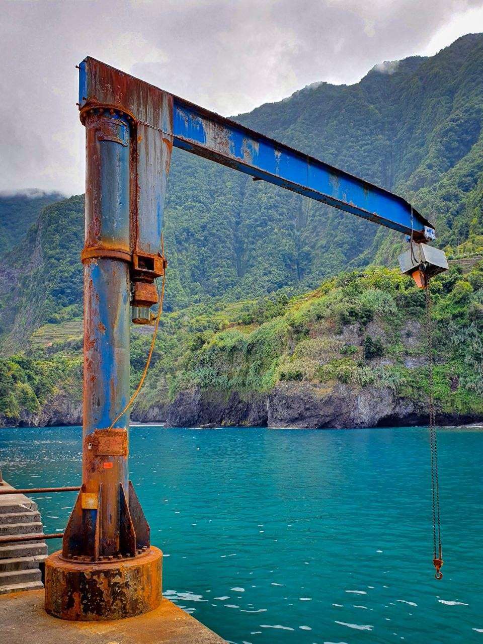 Industrial crane on Madeira harbor dock with turquoise water and green cliffs